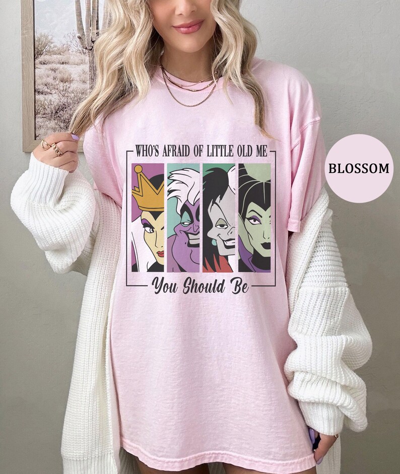 Puede incluir: Camiseta rosa claro con un gr&aacute;fico de cuatro villanos de dibujos animados y el texto "WHO'S AFRAID OF LITTLE OLD ME - YOU SHOULD BE". La camiseta tiene cuello redondo y mangas cortas.