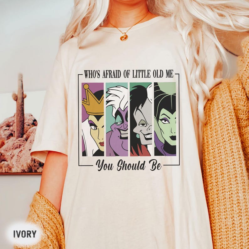 May include: Ivory t-shirt with a graphic of four Disney villains in a vertical panel design. The text "WHO'S AFRAID OF LITTLE OLD ME - You Should Be" is printed above and below the graphic. A casual wear item.