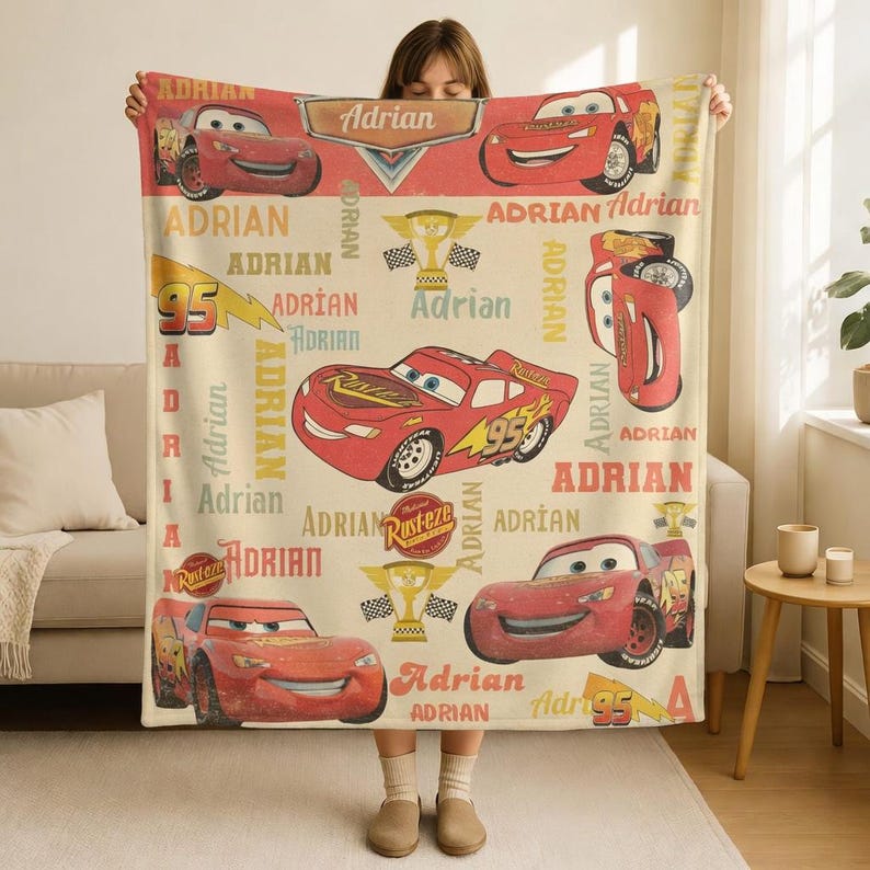 Op de afbeelding: Een beige deken met Lightning McQueen uit de film Cars. De deken heeft een herhalend patroon van het personage, het nummer 95 en de naam "Adrian" in rood en geel. Geschikt voor bed of bank.