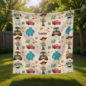 May include: A cream-colored blanket featuring cartoon characters from Toy Story and Monsters, Inc. The blanket has images of Woody, Buzz Lightyear, Sully, and Wall-E, along with the name "Lucas". The blanket is hanging outside.