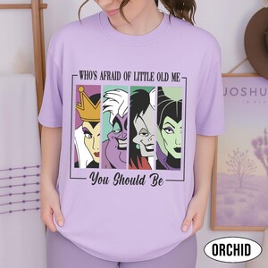 Puede incluir: Una camiseta de color lila con un gr&aacute;fico de cuatro villanos de Disney: la Reina Malvada, &Uacute;rsula, Cruella de Vil y Mal&eacute;fica. El texto "WHO'S AFRAID OF LITTLE OLD ME - You Should Be" est&aacute; impreso encima y debajo del gr&aacute;fico.