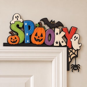 May include: A wooden door corner sign spelling SPOOKY in colourful letters. The S is green with a ghost, P is blue with stars, O is an orange jack-o'-lantern, O is purple, K is cream with stars, Y is red with a ghost, a black bat, and a spider web with a spider.