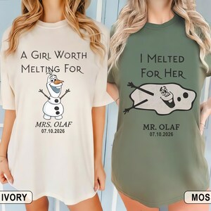 以下が含まれることがあります： 2枚のTシャツ。1枚はアイボリー、もう1枚はモスグリーンで、アナと雪の女王のオラフのデザイン。アイボリーのシャツには「A Girl Worth Melting For」と「Mrs. Olaf」と日付が書かれています。モスグリーンのシャツには「I Melted For Her」と「Mr. Olaf」と日付が書かれています。