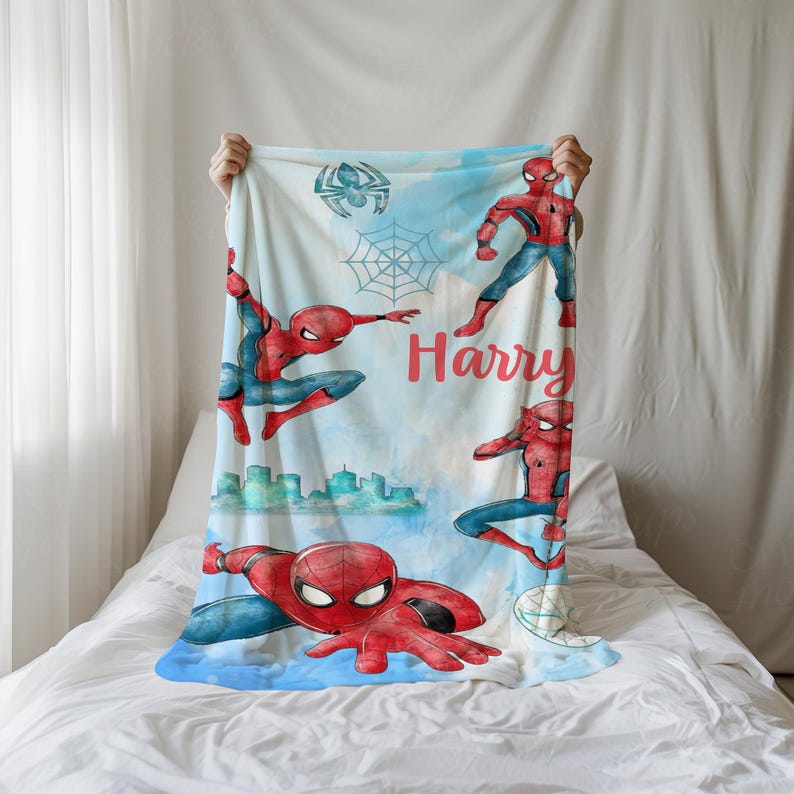 K&ouml;nnte beinhalten: Eine wei&szlig;e Decke mit einem Aquarelldesign von Spider-Man in verschiedenen Actionposen. Die Decke hat einen hellblauen Hintergrund mit einer Stadtlandschaft und dem Namen "Harry" in roter Schrift. Ein Spinnennetz und ein Spinnenemblem sind ebenfalls enthalten.