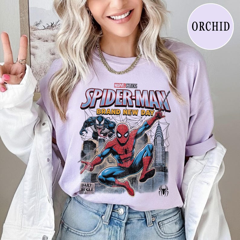 K&ouml;nnte beinhalten: Ein helllila T-Shirt mit einer Marvel Studios Spider-Man Grafik. Das Design zeigt Spider-Man in einer dynamischen Pose, den Text "SPIDER-MAN BRAND NEW DAY" und das Daily Bugle Logo. Das Shirt ist Teil der Orchid-Kollektion.