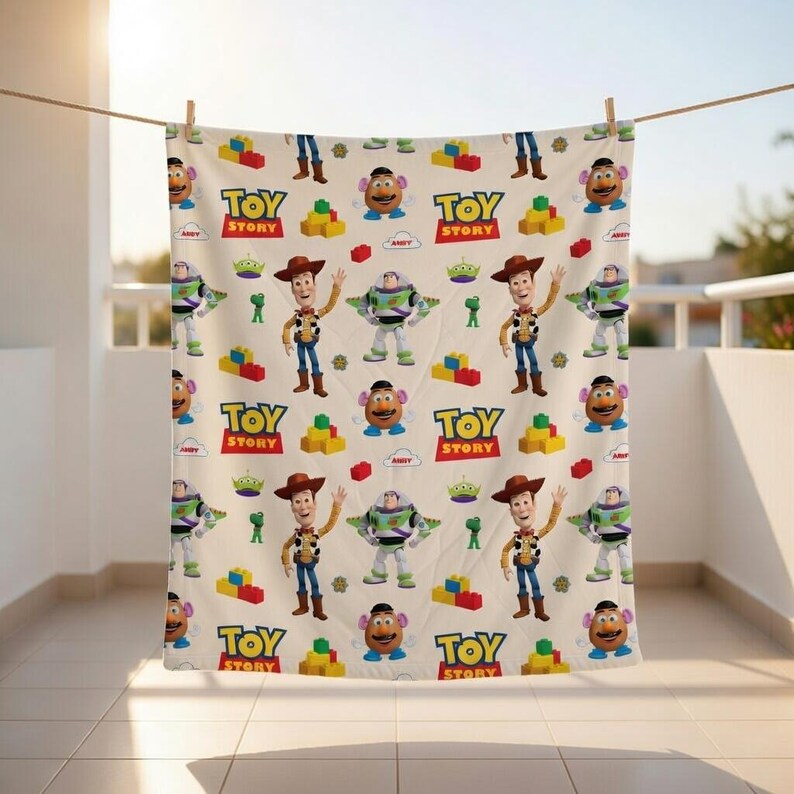 May include: A beige blanket featuring a repeating pattern of characters and elements from the animated film "Toy Story." The design includes Woody, Buzz Lightyear, Mr. Potato Head, green aliens, and building blocks, along with the "Toy Story" logo.