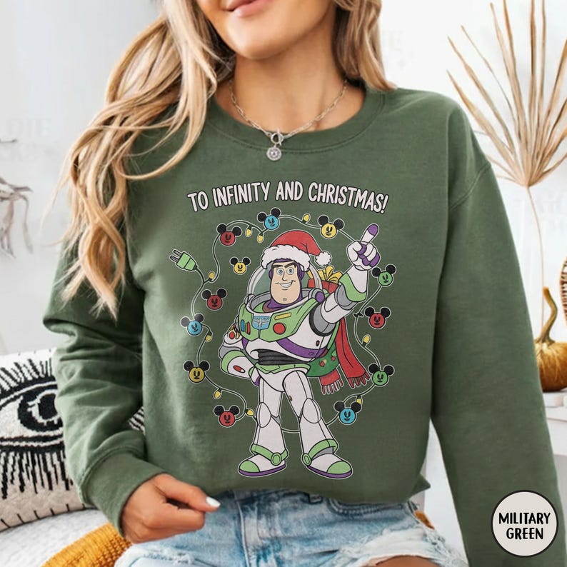May include: Military green crew neck sweatshirt with a graphic of Buzz Lightyear wearing a Santa hat, surrounded by Mickey Mouse-shaped Christmas lights. The text "TO INFINITY AND CHRISTMAS!" is printed above the graphic.