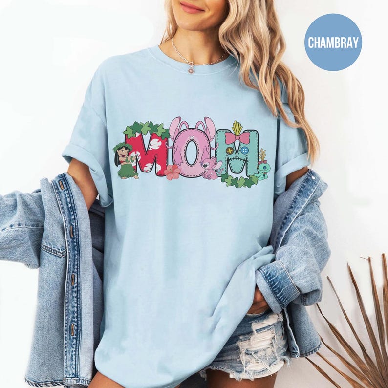 K&ouml;nnte beinhalten: Hellblaues T-Shirt mit dem Wort "MOM" in einem farbenfrohen Grafikdesign. Das "M" ist rot mit gr&uuml;nen Bl&auml;ttern, das "O" ist rosa mit Hasenohren und das "M" ist blau mit einer Schleife. Das Shirt hat einen l&auml;ssigen Stil.