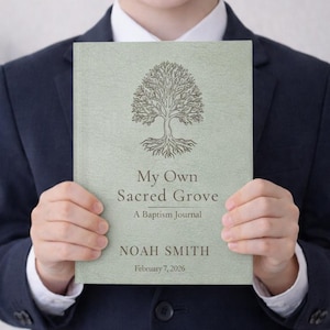May include: A baptism journal titled "My Own Sacred Grove" held by a person. The cover is a light green with a tree illustration and the text "A Baptism Journal", "Noah Smith", and "February 7, 2026". The person is wearing a navy blue suit.