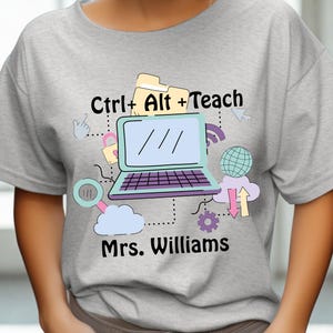 May include: A light gray t-shirt with the text "Ctrl + Alt + Teach" and "Mrs. Williams" printed on the front. The design includes a laptop, cloud, and other graphics. The shirt is labeled "Sport Grey".