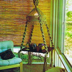May include: A macrame hanging table with a woven lampshade, a glass, a small potted plant, and a chair in a room with a bamboo blind and a window.