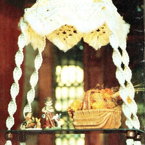 May include: A white macrame hanging with a woven basket filled with dried flowers, a small hourglass, and a stack of books on a glass shelf.