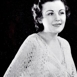 May include: A woman wearing a white lace shawl with a delicate pattern. The shawl is draped over her shoulders and tied at the front. She is wearing a white blouse underneath.