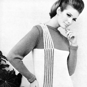 Puede incluir: Un suéter de punto con un diseño de bloques de color blanco y gris. El suéter tiene una franja vertical de detalle de punto en la parte delantera con pompones en la parte inferior.