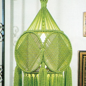 Puede incluir: Una lámpara colgante de macramé verde con un diseño circular y borlas. La lámpara está hecha de cordón anudado y tiene una bombilla en el interior.