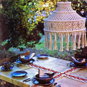 May include: A white macrame lampshade hangs over a wooden table set with blue and brown ceramic plates and bowls. The table is covered with a white and red crocheted table runner.