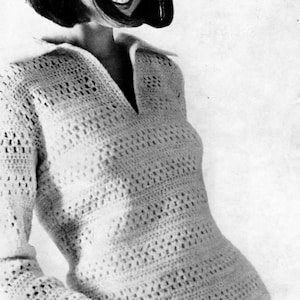 May include: A cream-colored, long-sleeved crochet dress with a V-neck collar. The dress has a textured, open-weave design. The image is a black and white photograph.