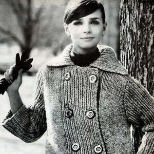 May include: A woman wearing a long, grey knitted cardigan with large buttons. The cardigan has a double-breasted closure and a collar.