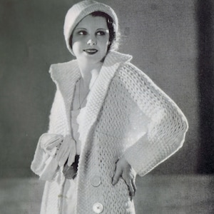 May include: A white knitted cardigan with a large collar and two buttons. The cardigan is long and has a loose fit. The model is wearing a white hat.