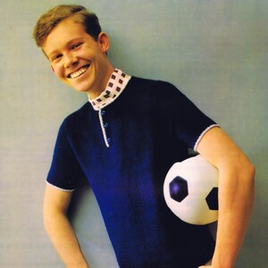 Puede incluir: Un polo de punto azul marino con cuello estampado y ribete blanco. La camisa tiene una tapeta de tres botones. Un balón de fútbol blanco y negro se sostiene en el brazo. La persona lleva pantalones de color claro.