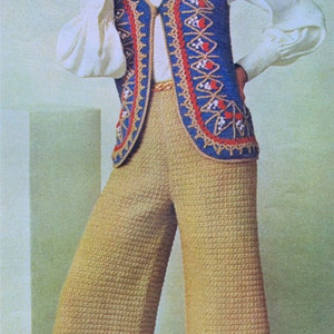 Peut inclure: Une femme portant un gilet crocheté bleu, rouge et blanc sur un chemisier à col roulé blanc et un pantalon crocheté beige.