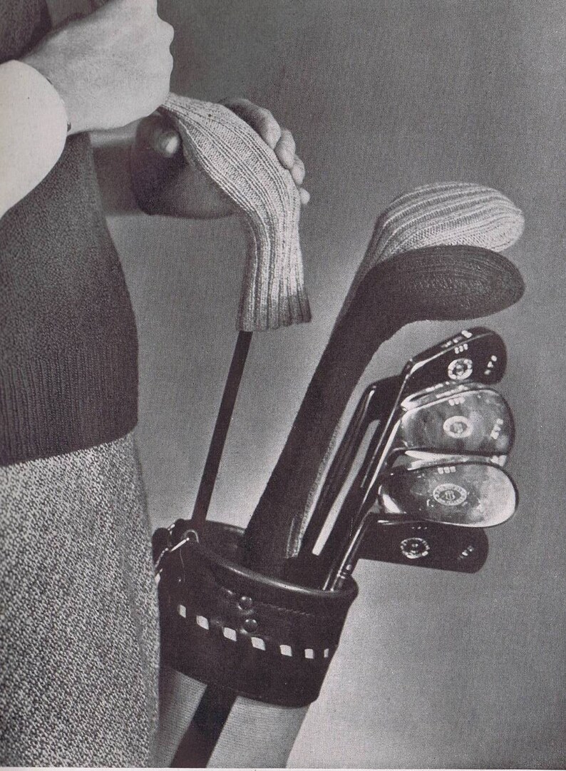 K&ouml;nnte beinhalten: Eine schwarze Ledertasche f&uuml;r Golfschl&auml;ger mit einer Rei&szlig;verschlusstasche und einem Trageriemen. Die Tasche ist gef&uuml;llt mit Golfschl&auml;gern, die jeweils mit einer wei&szlig;en gestrickten Schl&auml;gerkopf-Abdeckung versehen sind.