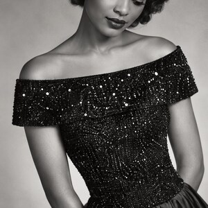 May include: A black off-the-shoulder blouse featuring dense bead and sequin embellishments across the bodice and sleeves. The garment has a fitted silhouette and a straight neckline. The text Beaded Sequin Blouse is printed at the bottom.