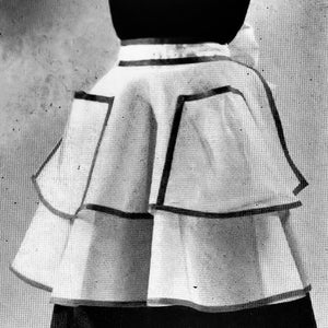 May include: A white apron with black trim and two large pockets. The apron has a ruffled bottom.