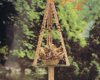 May include: A macrame plant hanger with a decorative basket holding dried flowers. The plant hanger is suspended from a rope and features wooden beads. The text "Macrame Elegance II" is visible at the top, and "Belle Pensée" at the bottom.