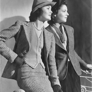 May include: Two women wearing hats and patterned jackets. The woman on the left is wearing a brown hat and a tweed jacket with a matching skirt. The woman on the right is wearing a black hat and a gray tweed jacket.