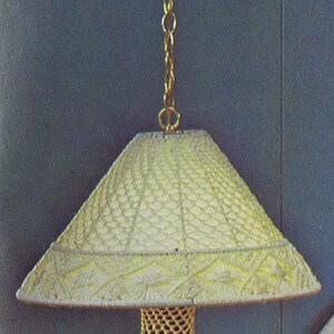 May include: A white crocheted lampshade hangs from a gold chain. The lampshade has a woven pattern and a round, open bottom. The lampshade is attached to a brown wooden base.