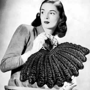 May include: A black and white photograph of a vintage, intricately crocheted garment. The garment has a scalloped edge and a detailed, textured pattern. The piece is held by a person wearing white gloves, suggesting a focus on craftsmanship and vintage fashion.