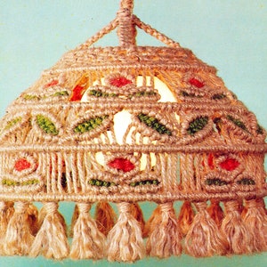 May include: A macrame lampshade with a beige, green and red pattern. The lampshade has a fringe border and is made of natural fibres.