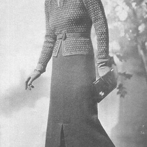 May include: A black and white photo of a woman wearing a fitted, patterned sweater dress with a belt and a hat. She is holding a small purse in her right hand.