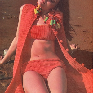May include: A woman wearing a crocheted bikini top and bottom with a matching crocheted cardigan. The cardigan has pom-poms on the edges. The bikini is a bright orange color.
