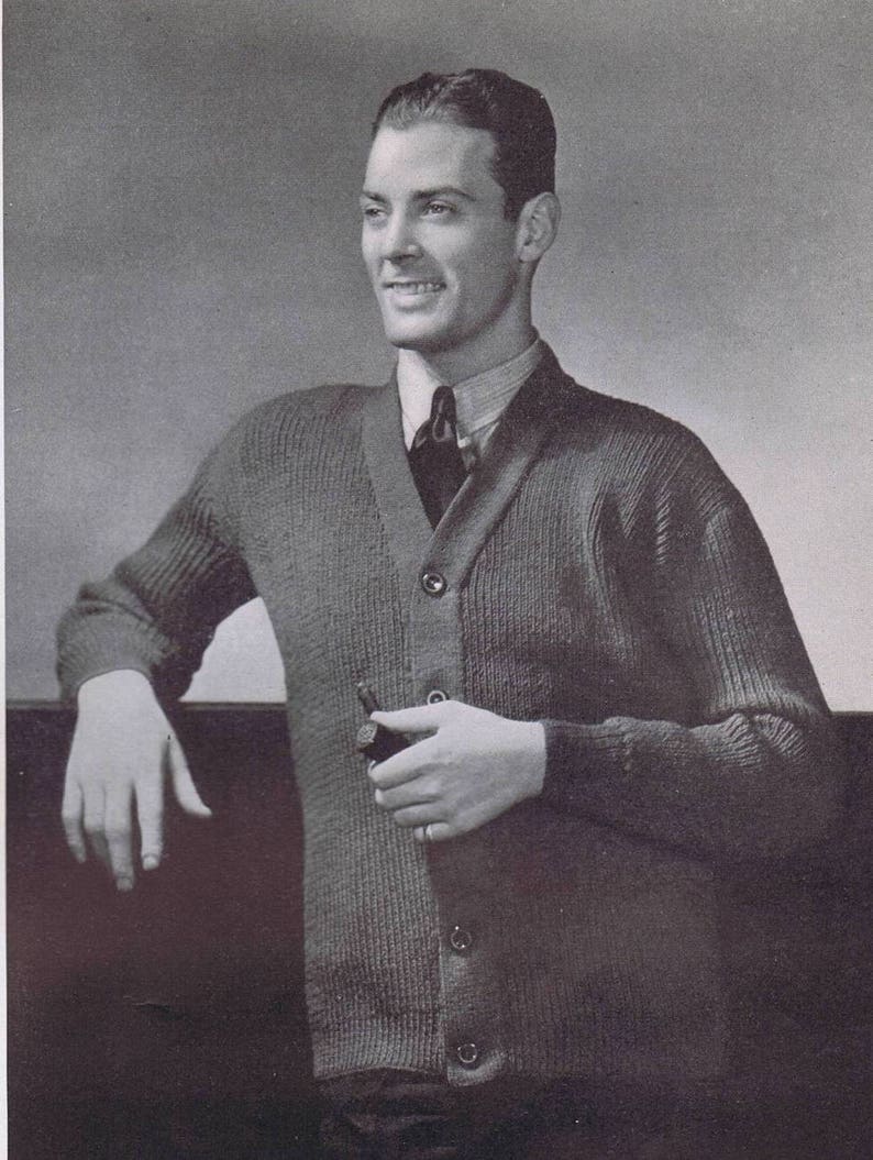 K&ouml;nnte beinhalten: Ein Schwarzwei&szlig;foto eines Mannes, der einen dunkelgrauen Strickpullover mit Kn&ouml;pfen und einer dunklen Krawatte tr&auml;gt. Er h&auml;lt eine Pfeife in seiner rechten Hand.