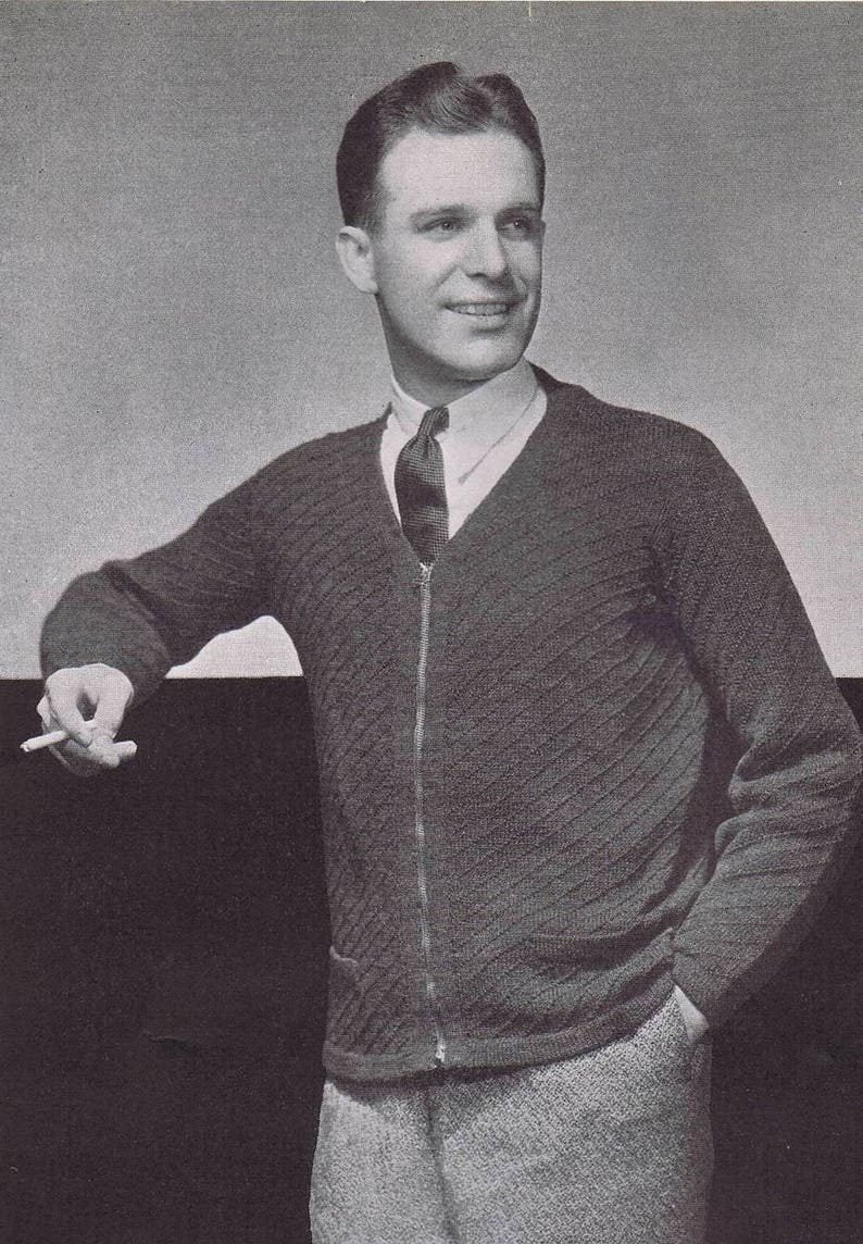 K&ouml;nnte beinhalten: Ein Schwarzwei&szlig;foto eines Mannes, der einen dunkelgrauen Strickpullover mit Rei&szlig;verschluss und einer dunklen Krawatte tr&auml;gt. Er l&auml;chelt und h&auml;lt eine Zigarette in seiner rechten Hand.