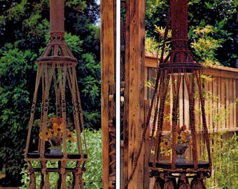 May include: Two macrame plant hangers, one in natural tones and the other in brown, each suspended from a wooden structure. The hangers feature a cylindrical top, a circular shelf, and decorative tassels. Each holds a vase of flowers.