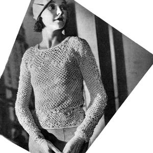 Puede incluir: Imagen en blanco y negro de un top de ganchillo vintage con mangas largas y boina. El top calado presenta un motivo floral en la cintura. La boina y el top probablemente están hechos de un material suave y transpirable.