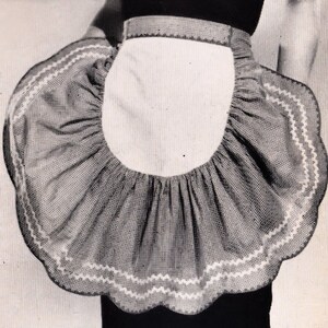 Pode incluir: Um avental de estilo vintage com um bolso central branco e uma borda ondulada e com babados. O tecido do avental tem um padrão de listras sutis, e as bordas são aparadas com uma costura em zigue-zague branca. O avental é projetado para ser usado na cintura.