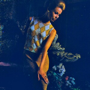 May include: A woman wearing a sleeveless top with a diamond pattern in gold and white. The top is beaded and the woman is wearing a gold skirt.