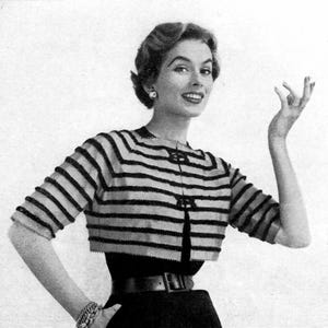 May include: A black and tan striped bolero jacket with short sleeves. The jacket has a round neckline and is fastened with three decorative buttons. The model is wearing a black skirt and a wide black belt.