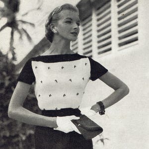 Può includere: Fotografia in bianco e nero di una donna con un top a fantasia bianco e nero con maniche corte. Il top ha uno scollo nero e piccoli motivi a forma di croce. Indossa anche una gonna scura, guanti bianchi e tiene in mano una piccola borsetta.