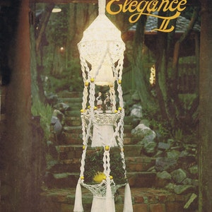 May include: A book cover for a macrame pattern book titled "Macrame Elegance II". The cover features a white macrame hanging planter with three tiers and yellow beads. The book cover also includes the text "Basic to Advanced Designs Including Macrame Necklaces" and "De Lune".