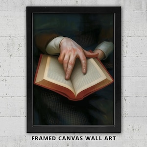 May include: Framed canvas wall art featuring a classic painting of a person's hand pointing at an open book. The book has a red cover and the pages are off-white. The artwork is set against a dark background.