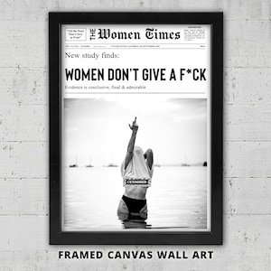 Può includere: Opera d'arte da parete su tela incorniciata in bianco e nero. L'opera presenta un titolo in stile giornale che recita: "WOMEN DON'T GIVE A F*CK." Sotto il titolo c'è una foto in bianco e nero di una persona in acqua che fa un gesto osceno.