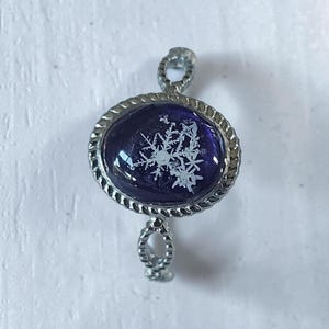 Peut inclure: Bague argentée ornée d'un cabochon ovale bleu foncé avec un motif de flocon de neige blanc. La bague présente un bord torsadé en forme de corde et une monture torsadée.