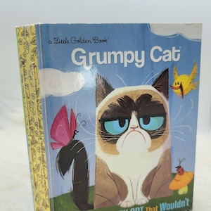May include: A Little Golden Book titled "Grumpy Cat: The Little Grumpy Cat That Wouldn't". The cover features a cartoon illustration of a grumpy cat with blue eyes and a frown. The cat is surrounded by a butterfly, a bird, and a ladybug.