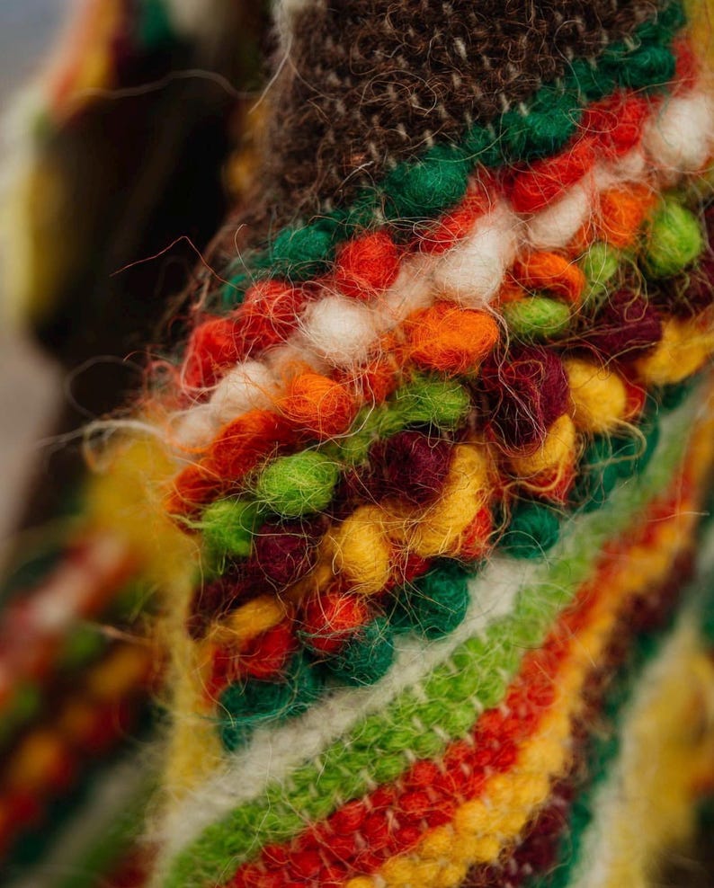 May include: Close-up of a vibrant, textured textile featuring a mix of colors. The design incorporates a variety of textures and hues, including red, orange, green, yellow, and white. The textile has a fuzzy, handmade appearance, suggesting a craft item.