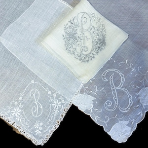 May include: Several white handkerchiefs with embroidered floral designs and the letter "B". One handkerchief has a scalloped edge, and another has a lace trim. The embroidery is in a light gray color.